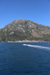 A motorboat sails on the sea against the backdrop of the town of Perast in the Bay of Kotor, mountains