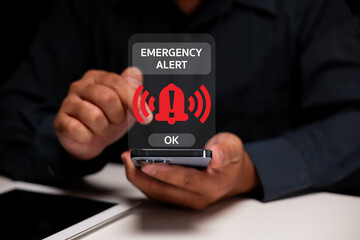 A person holding a smartphone with an emergency alert notification displayed on the screen,...