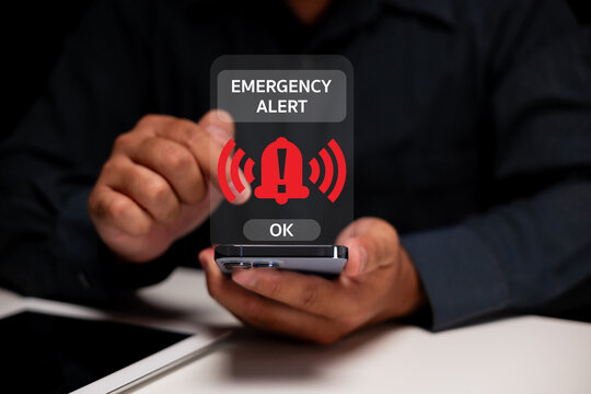 A person holding a smartphone with an emergency alert notification displayed on the screen, signaling urgent information. - Powered by Adobe