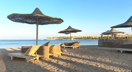 A serene beach scene in Egypt by the Red Sea. Sun loungers and straw umbrellas are set on the sandy...