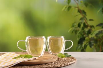 Tasty green tea in glass cups and leaves on white marble table outdoors, space for text
