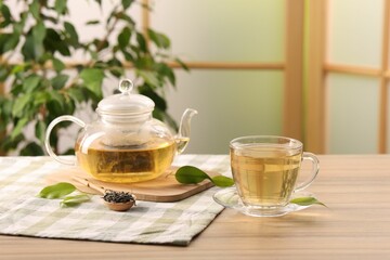 Tasty green tea in glass cup, teapot, brew and leaves on wooden table indoors