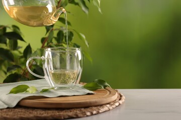 Pouring tasty green tea into cup at white marble table outdoors, closeup. Space for text