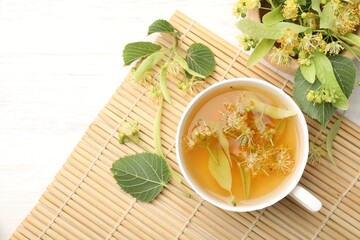 Fresh linden tea in cup and flowers on white wooden table, flat lay. Space for text