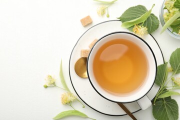Tasty linden tea in cup, spoon, sugar cubes, leaves and flowers on white table, flat lay. Space for text