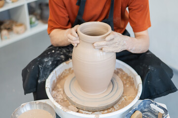 Close-up of a potter's hands making a ceramic vase on a potter's wheel. 
