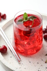 Tasty cherry soda with ice cubes, mint and berries on white table, closeup