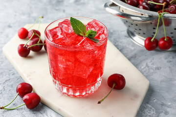 Tasty cherry soda with ice cubes, berries and mint in glass on grey textured table, closeup
