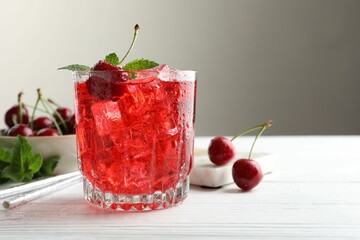 Tasty cherry soda with ice cubes, berries and mint in glass on white wooden table, closeup. Space...