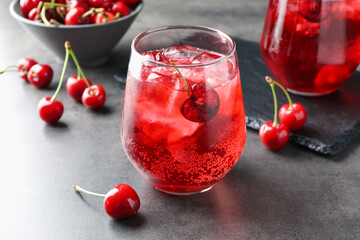 Tasty cherry soda with ice cubes and berries in glasses on grey table, closeup