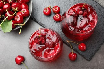 Tasty cherry soda with ice cubes and berries in glasses on grey table, flat lay