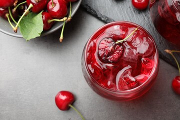 Tasty cherry soda with ice cubes and berries in glasses on grey table, flat lay