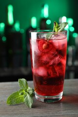 Tasty cherry soda water with ice cubes, berry and mint in glass on wooden table against blurred green background, closeup