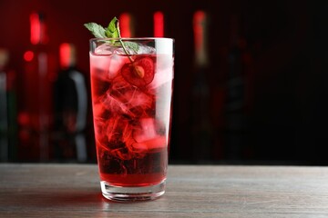 Tasty cherry soda water with ice cubes, berry and mint in glass on wooden table against blurred background
