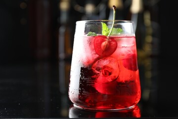 Tasty cherry soda water with ice cubes, berry and mint in glass on mirror table against blurred...
