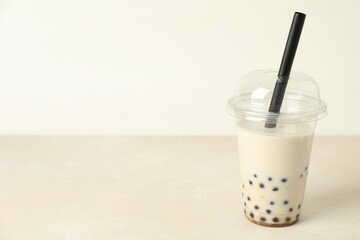 Tasty milk bubble tea in plastic cup on beige table, space for text