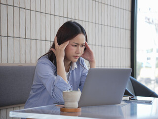A stressed young woman sits in front of her laptop in a cafe.