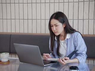 A young Asian woman in casual clothes looking at her laptop computer with concern at a cafe.