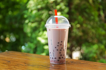 Tasty milk bubble tea in plastic cup on wooden table