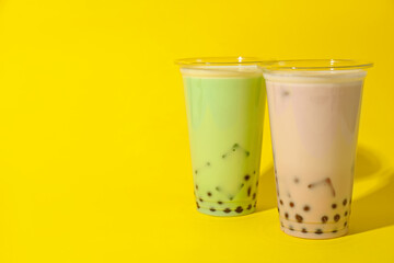 Tasty milk bubble tea in plastic cups on yellow background. Space for text