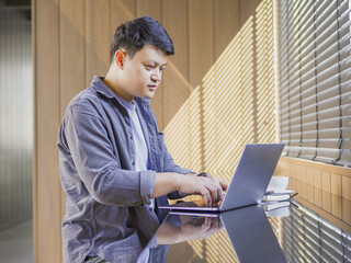 Young Asian man sitting working on computer with white coffee cup in cafe