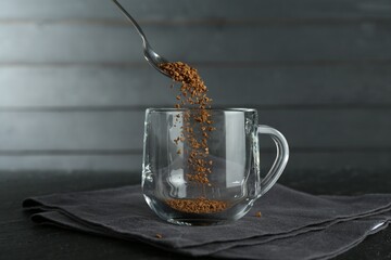 Putting instant coffee into cup at black table, closeup