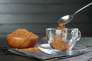 Putting instant coffee into cup at black table, closeup