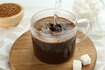Pouring hot water into cup with instant coffee at light table, closeup