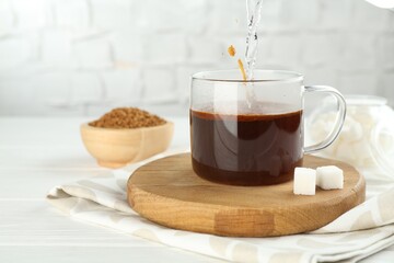 Pouring hot water into cup with instant coffee at light table, closeup