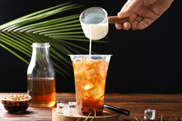 Woman pouring milk into bubble tea at wooden table, closeup