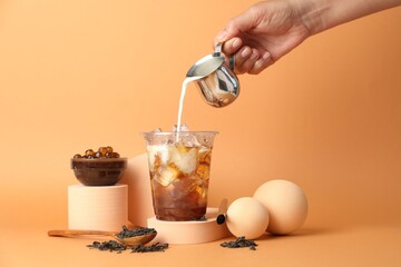 Woman pouring milk into bubble tea on orange background, closeup