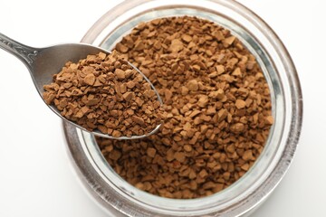 Spoon with instant coffee over bowl against white background, top view