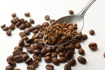 Spoon with instant coffee and beans on white table, closeup