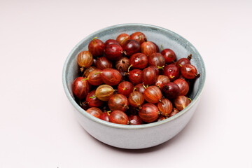 Fresh gooseberries with water drops in blue ceramic bowl, isolated on plain purple background, banner