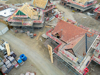 Drone view of roof timbers being installed on a modern, detached home on a typical housing estate in the UK. The roofs are seen in various levels of construction.