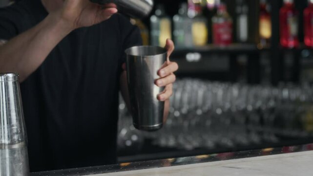 Cropped shot of male tattooed bartender adding ice in shakers and preparing cordial glass in modern restaurant