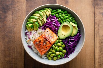 Top view of vibrant Asian fusion bowl with jasmine rice, seared salmon, avocado, edamame, red cabbage, sesame seeds, and ginger dressing in a deep ceramic bowl on light wooden table with copy space.  