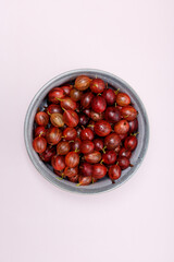 Fresh gooseberries with water drops in blue ceramic bowl, top view, isolated on plain purple background, banner