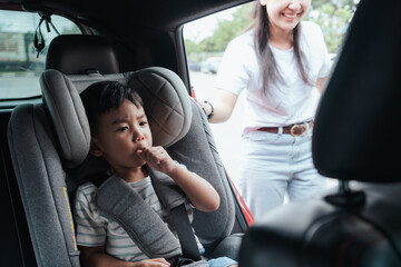Little boy in car seat sucking lollipop as mother opens the car door. Realistic lifestyle travel...