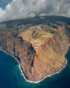 Aerial view of rugged cliffs meet the vast ocean under a cloudy sky, showcasing the dramatic landscape of Ponta do Pargo, Madeira, Portugal.