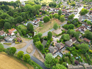 Picturesque drone view of a typical British rural village showing the village green surrounded by houses and a small pond.  Seen near a road junction leading to the village.