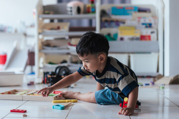 Asian boy playing with colorful wooden educational toy at home. Concentrated child engaged in hands-on learning activity. Homeschooling, early development, and independent playtime concept.