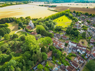Pretty aerial view of a typical rural British village seen within lush trees and prime arable land. A church tower in the distance can be seen being renovated.