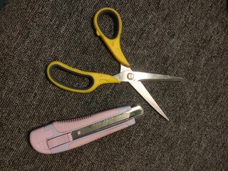 Yellow scissors and a pink utility knife lie on a textured surface, essential tools for crafting, office work, or DIY projects.