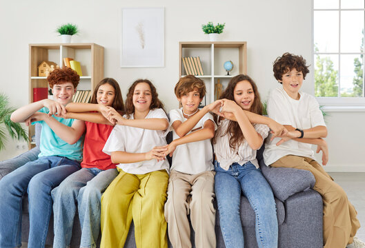 Smiling friends, diverse happy teen group team of cheerful classmates, sitting together doing group arm wave gesture, commonly hands use to show unity, having fun enjoying, engaged in teambuilding