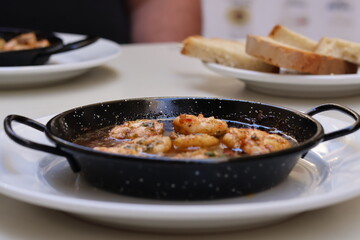 Gambas Pil Pil Spanish dish served in traditional cast iron pan ,white plate on table top down photo