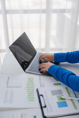 Laptop at Work: A close-up view of hands typing on a laptop keyboard amidst financial documents on...