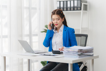 Obraz premium Portrait of beautiful businesswoman talking on the phone and working on laptop while sitting in office.