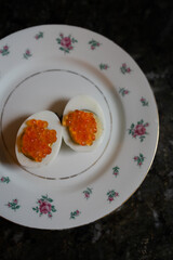 Unique presentation of deviled eggs topped with bright orange caviar on an elegant floral plate