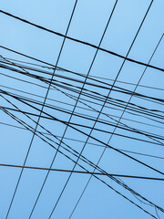 Tangled Power Lines Crisscross Against a Clear Blue Sky in a Chaotic Urban Overhead Utility Network
